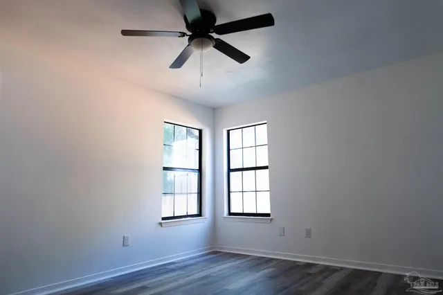 an empty room with wooden floor ceiling fan and windows