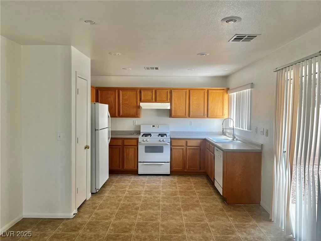 3153 Amari Avenue Las Vegas, NV 89141 - Photo 7 of 21 Kitchen with white appliances, light countertops, under cabinet range hood, brown cabinets, and recessed lighting