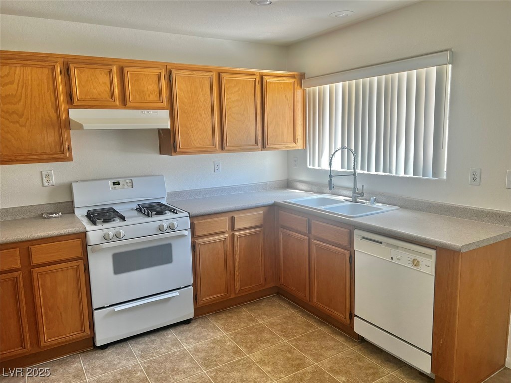 3153 Amari Avenue Las Vegas, NV 89141 - Photo 9 of 21 Kitchen featuring white appliances, under cabinet range hood, light countertops, brown cabinetry, and light tile patterned flooring