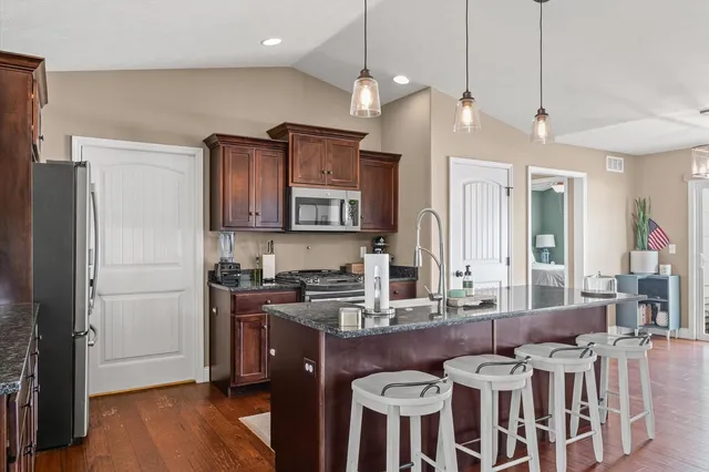 a kitchen with stainless steel appliances granite countertop a sink a stove a refrigerator and island with wooden floor