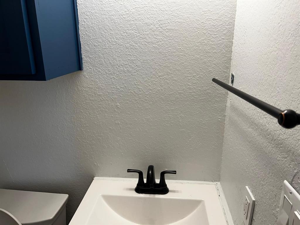 2025 County 1415 Road Bonham, TX 75418 - Photo 10 of 25 White sink with a matte black faucet, dark blue cabinetry, and a dark metal towel bar