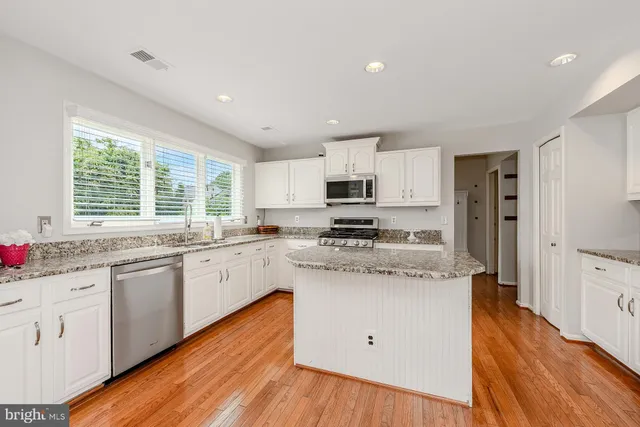 a kitchen with stainless steel appliances granite countertop wooden cabinets a refrigerator a sink a stove a center island and a wooden floor