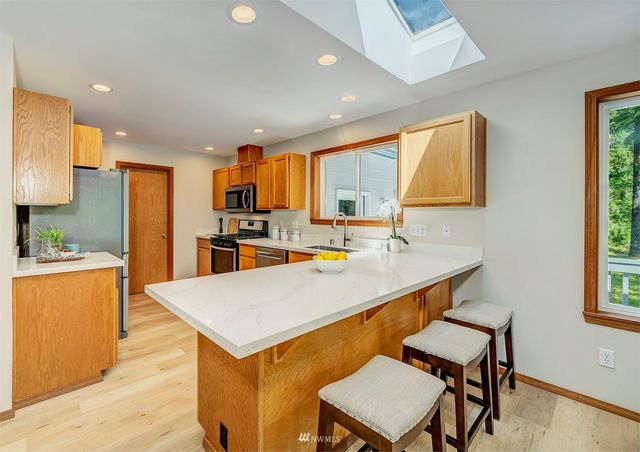 a kitchen with stainless steel appliances kitchen island granite countertop a refrigerator a stove top oven a sink dishwasher and white cabinets with wooden floor