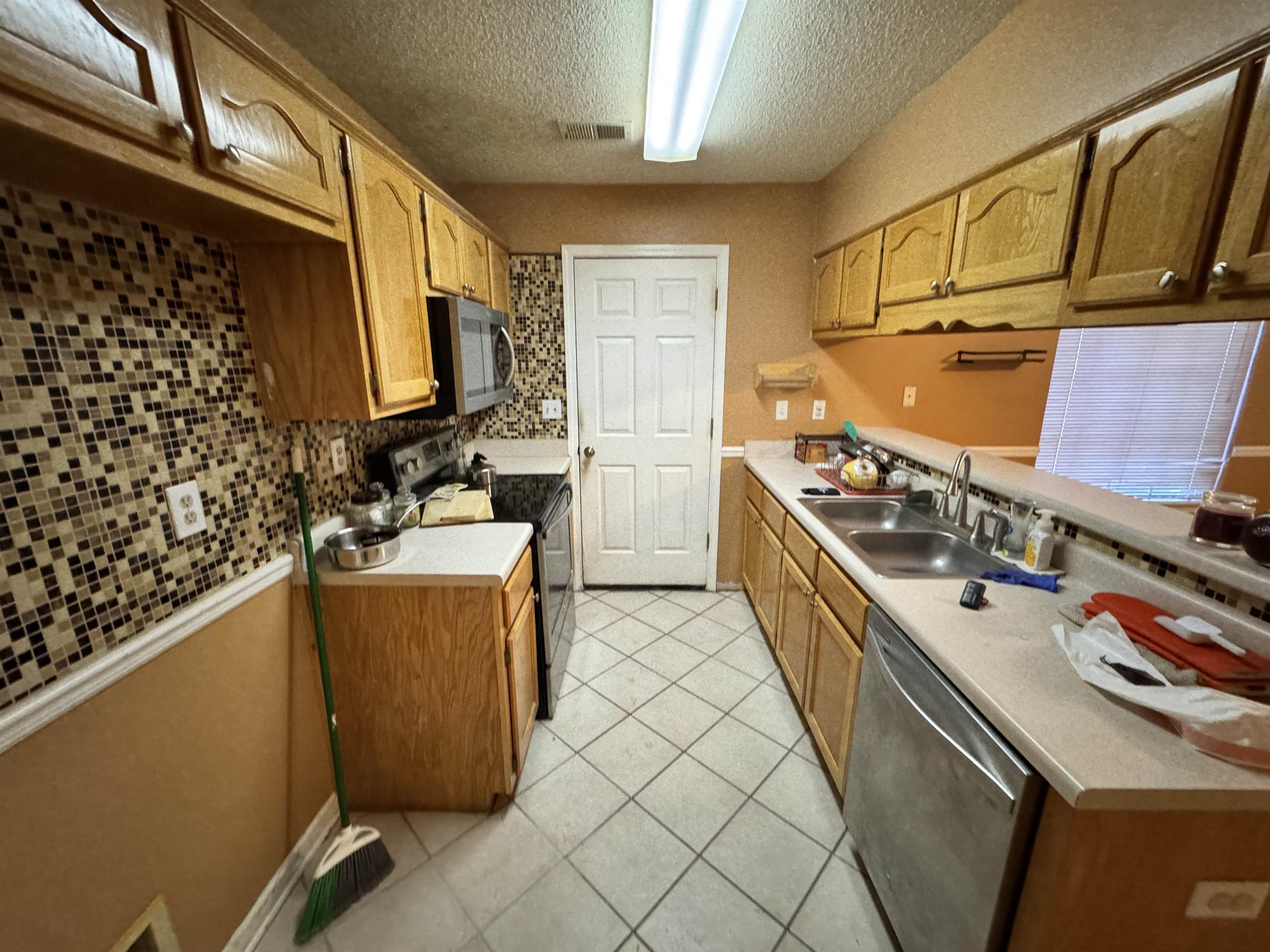 6912 Pleasantwood Road Memphis, TN 38141 - Photo 3 of 20 Kitchen featuring stainless steel appliances, light countertops, light tile patterned flooring, a textured ceiling, and wood finish cabinetry