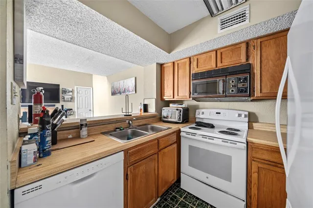 a kitchen with stainless steel appliances granite countertop a stove top oven a sink a refrigerator and white cabinets with wooden floor