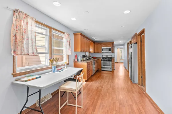 a kitchen with stainless steel appliances granite countertop a stove top oven a refrigerator a dining table and chairs with wooden floor