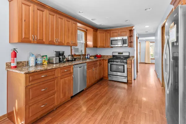 a kitchen with stainless steel appliances granite countertop wooden cabinets a refrigerator a sink a stove and a wooden floors