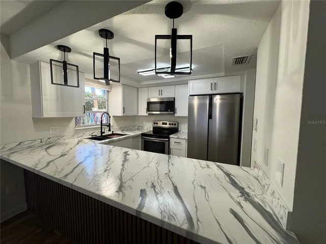 a kitchen with stainless steel appliances granite countertop a refrigerator a stove and a sink with wooden floor