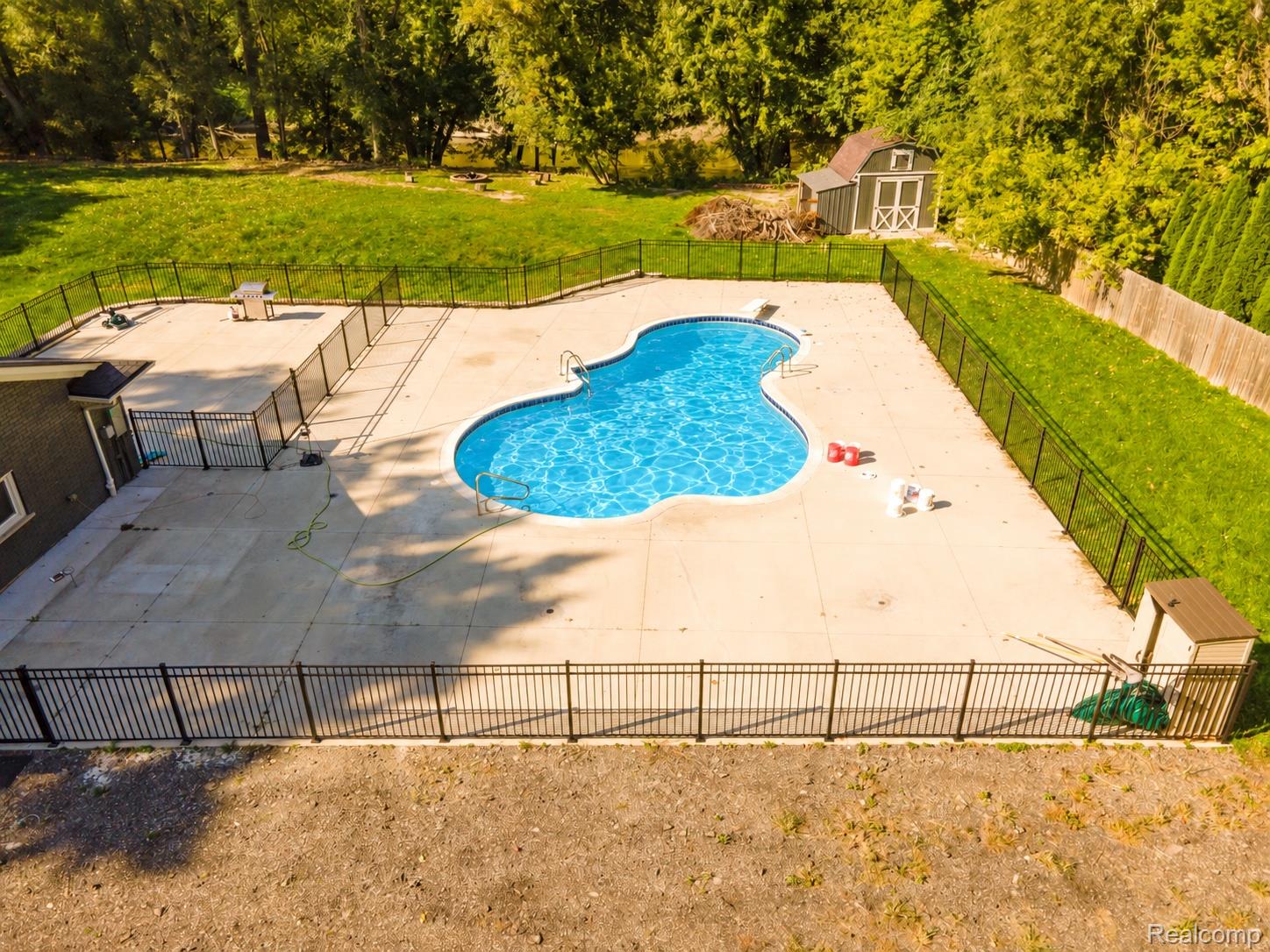 15879 Millar Road Clinton Township, MI 48036 - Photo 51 of 65 Kidney-shaped swimming pool with surrounding concrete patio, enclosed by black fencing