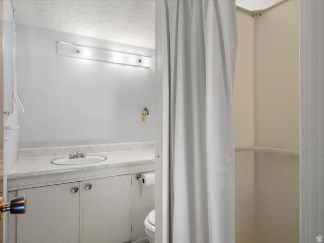 85 B Street, Unit 22 St. Charles, ID 83272 - Photo 26 of 35 Bathroom featuring a single vanity with a white countertop and integrated sink, white cabinetry, overhead bar lighting, and a shower area with a white curtain