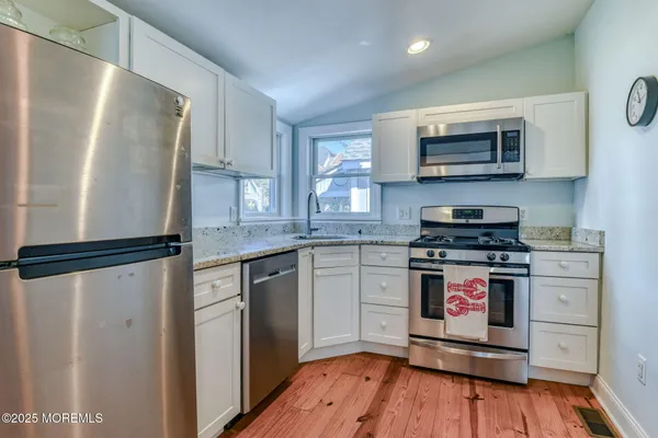 a kitchen with stainless steel appliances granite countertop a refrigerator a stove top oven a sink and dishwasher with wooden floor