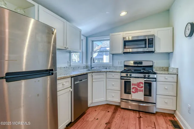 a kitchen with stainless steel appliances granite countertop a refrigerator a stove top oven a sink and dishwasher with wooden floor