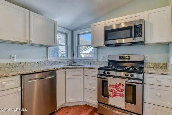 a kitchen with stainless steel appliances granite countertop a stove top oven a sink dishwasher and white cabinets with wooden floor