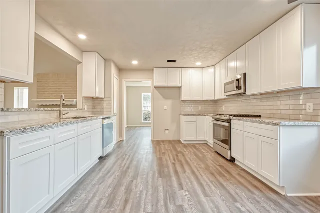 a large kitchen with granite countertop a large counter top a sink stainless steel appliances and cabinets