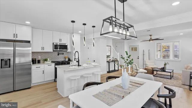 a kitchen with stainless steel appliances kitchen island granite countertop a stove a sink a refrigerator white cabinets and couches with wooden floor