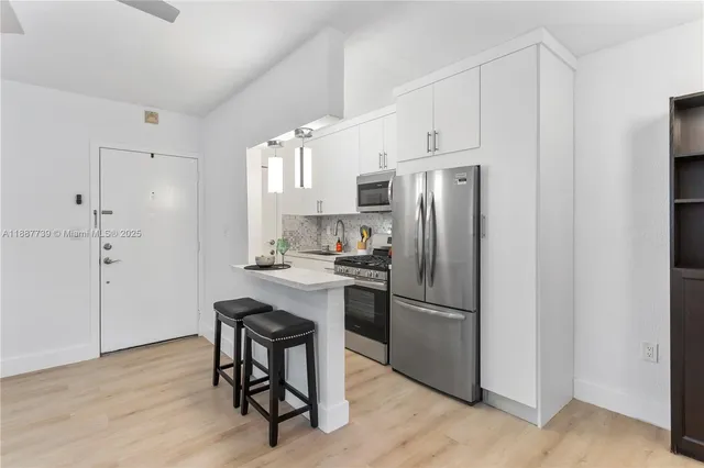 a kitchen with stainless steel appliances granite countertop a refrigerator a stove a sink and white cabinets with wooden floor