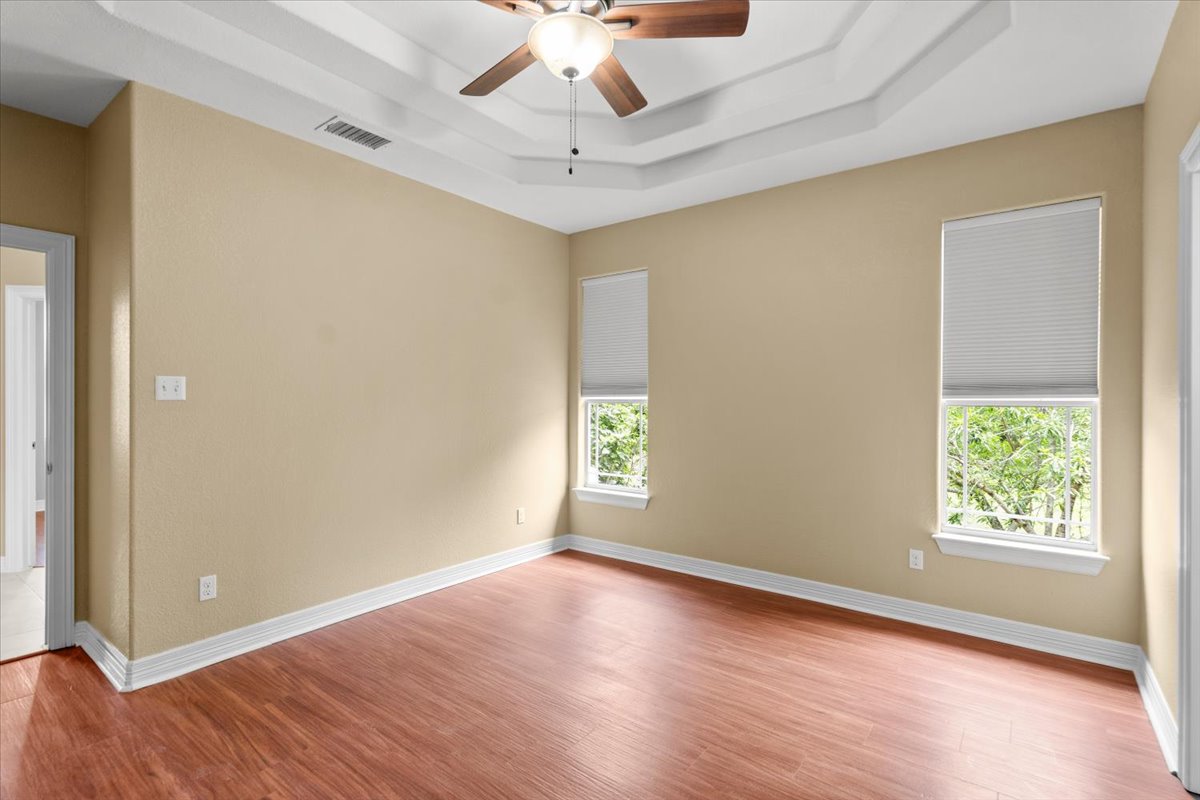 437 Balch Road Elgin, TX 78621 - Photo 13 of 37 A well-lit bedroom features rich hardwood flooring and a dramatic tray ceiling with a functional ceiling fan.