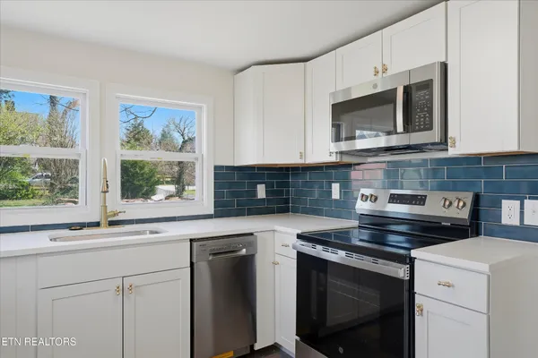 a kitchen with granite countertop white cabinets appliances and a window