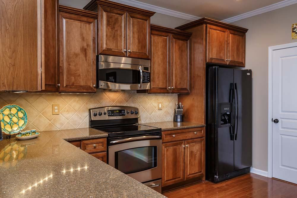 9154 Wooden Road Raleigh, NC 27617 - Photo 6 of 25 Upgraded cabinets, knobs & pulls throughout the home, w/cascading uppers, deep drawer storage, roll-out lower shelves & trash can in the kitchen! Quartz countertops, decorative backsplash, crown moulding, stainless appliances & custom pantry shelving!