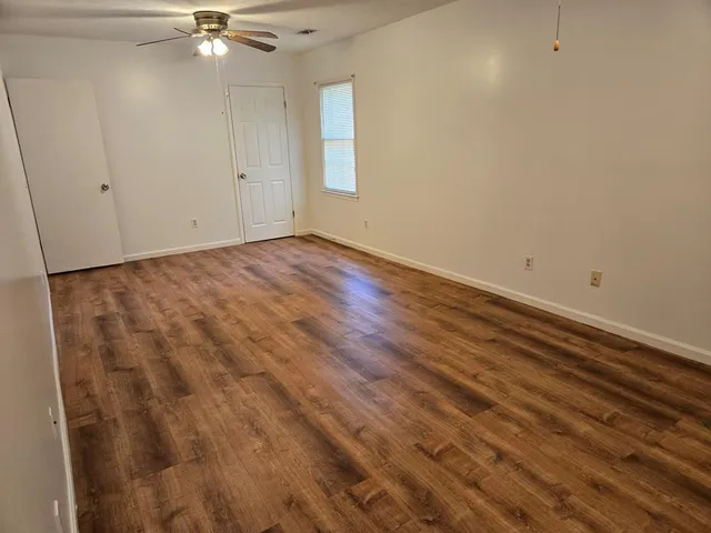 a view of an empty room with wooden floor and a bathroom
