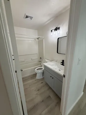 a view of a hallway with wooden floor and a bathroom