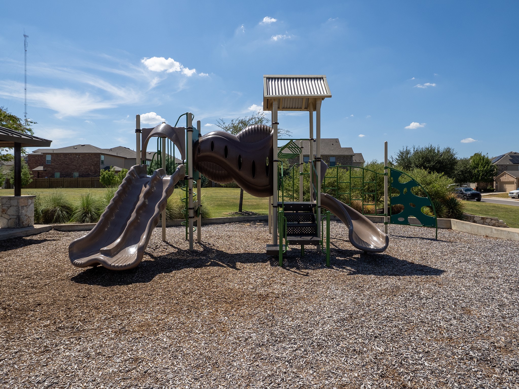 104 Rocroi Drive Georgetown, TX 78626 - Photo 38 of 40 A modern outdoor play structure stands on a wood-chip surface under a blue sky.