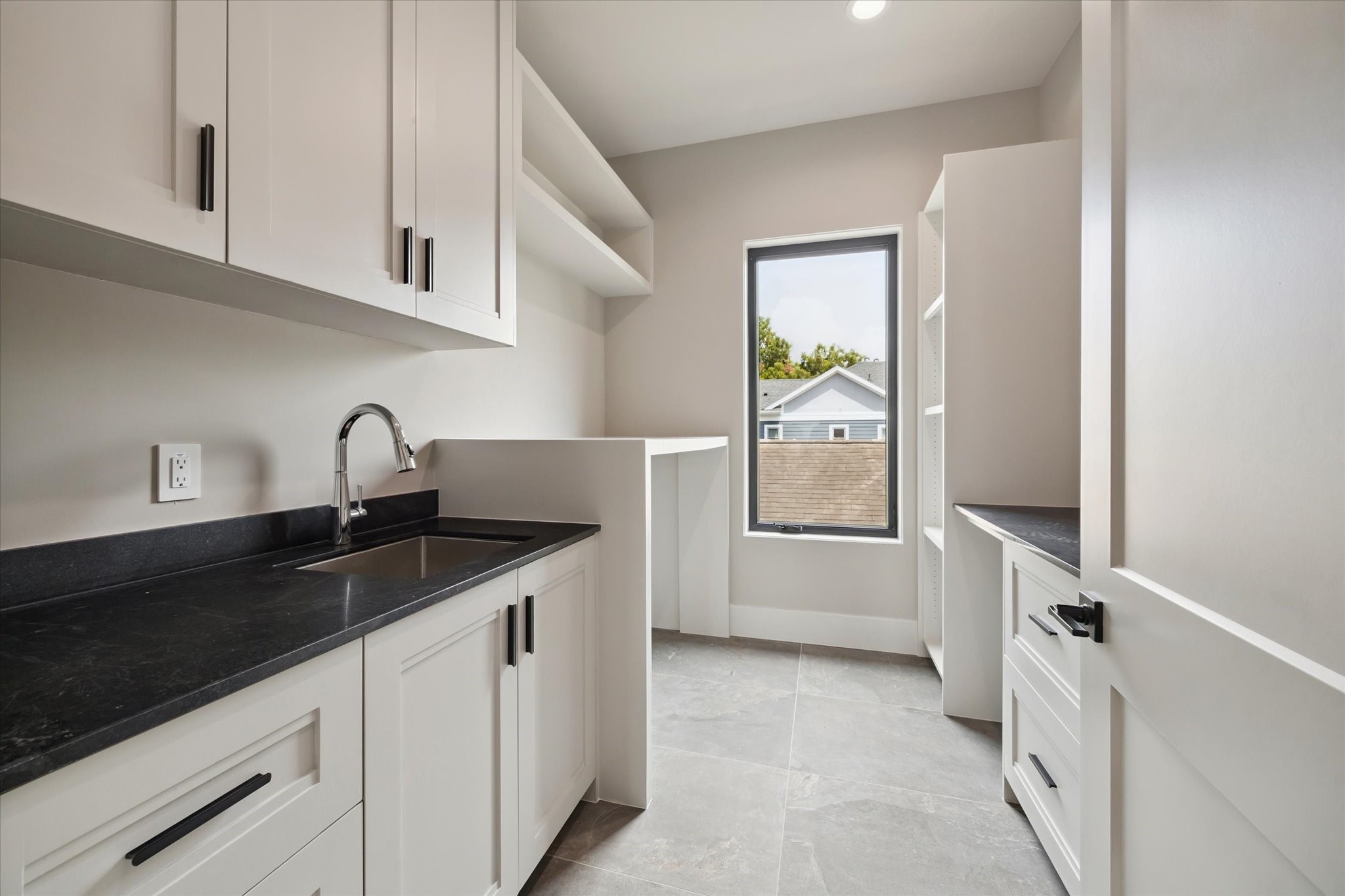 2120 Branard Street Houston, TX 77098 - Photo 28 of 33 The utility room features sleek cabinetry, quartz counters, and a deep stainless-steel sink. Open shelving, built-in storage, and a large window bringing in natural light make it both practical and inviting.