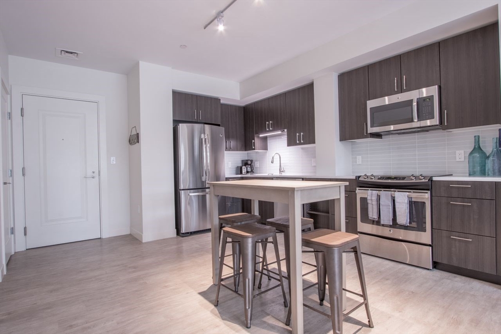 900 Beacon Street, Unit 408 Boston, MA 02215 - Photo 6 of 12 a kitchen with stainless steel appliances granite countertop a stove a sink a refrigerator with a dining table and chairs