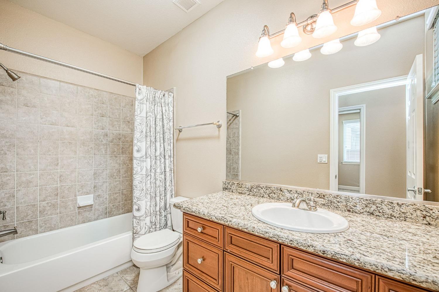 2267 Graybark Avenue Clovis, CA 93619 - Photo 29 of 42 a bathroom with a granite countertop sink a toilet a mirror a bathtub and shower