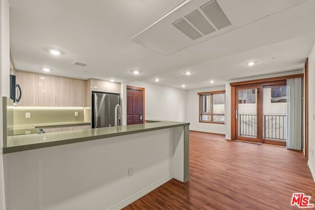 a living room with stainless steel appliances wooden floors and kitchen view