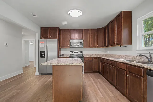 a kitchen with stainless steel appliances granite countertop a refrigerator a stove top oven a sink and dishwasher with wooden floor