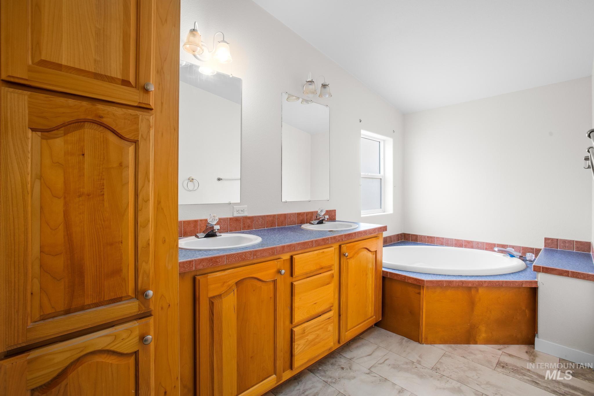 15190 Oasis Road Caldwell, ID 83607 - Photo 22 of 36 Dual vanity with integrated sinks, wood-finish cabinetry, and a built-in corner soaking tub
