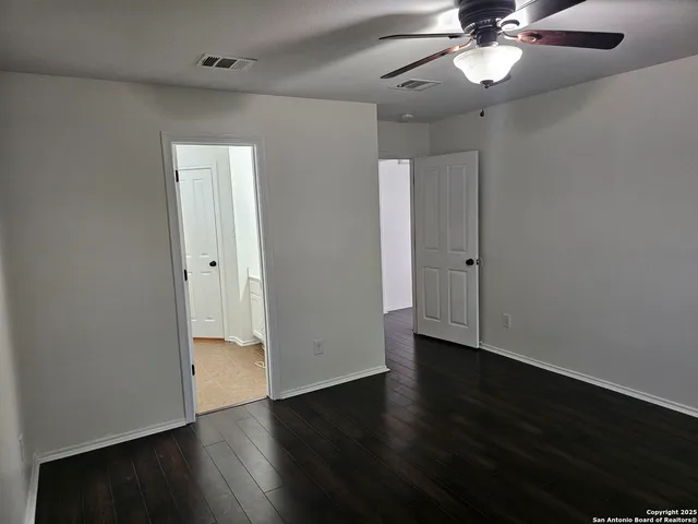 an empty room with wooden floor fan and windows
