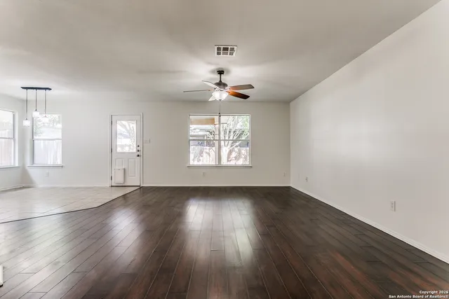 an empty room with wooden floor chandelier fan and windows