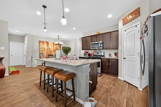 a kitchen with stainless steel appliances granite countertop a refrigerator a stove top oven a sink dishwasher and a dining table with wooden floor