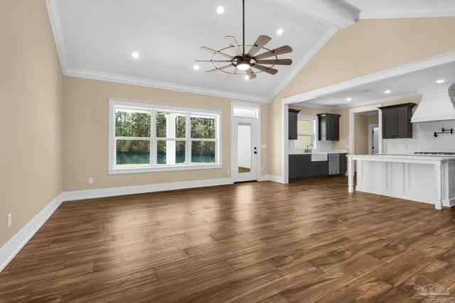 a view of an empty room with wooden floor and a kitchen