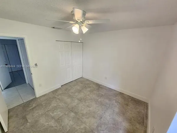 an empty room with a chandelier fan and view of bathroom