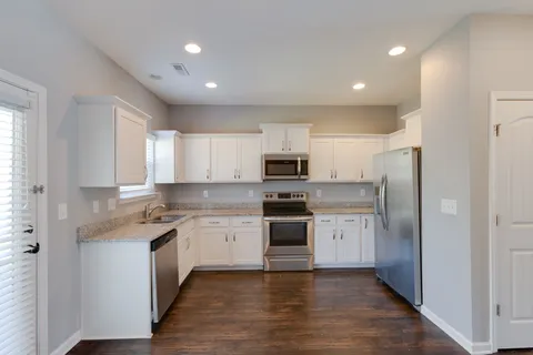 a kitchen with stainless steel appliances granite countertop a refrigerator a sink dishwasher a stove and white cabinets with wooden floor
