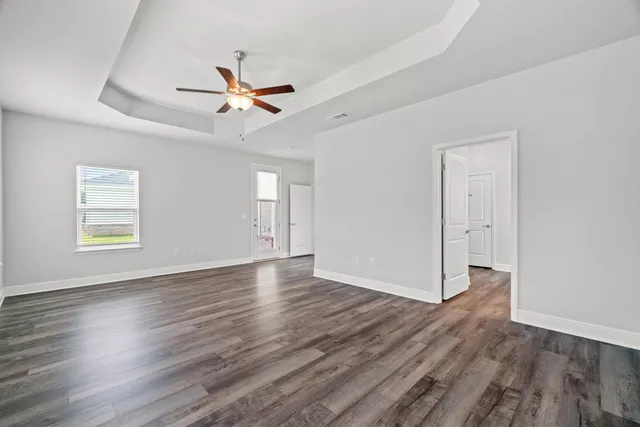 an empty room with wooden floor ceiling fan and windows