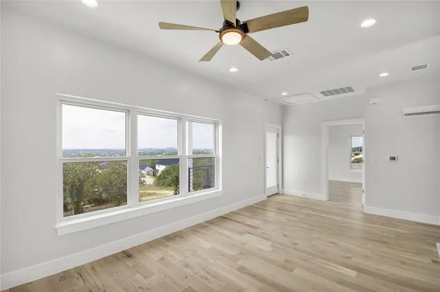 an empty room with wooden floor fan and windows