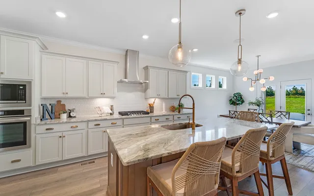 a kitchen with stainless steel appliances granite countertop a stove top oven a sink a dining table and chairs with white cabinets