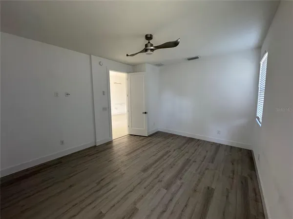 an empty room with wooden floor a ceiling fan and kitchen view