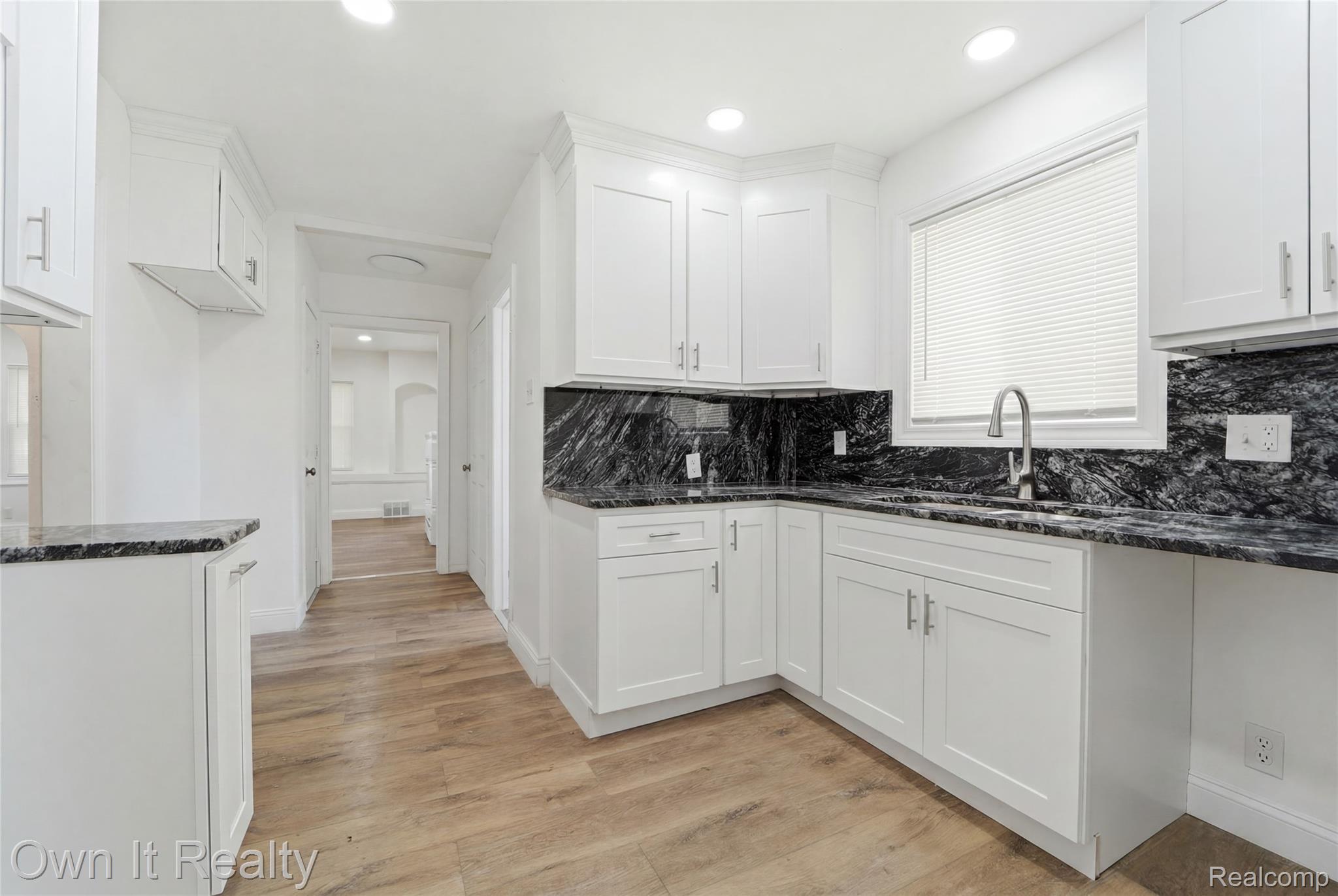 17351 Appoline Street Detroit, MI 48235 - Photo 11 of 34 Bright kitchen featuring white shaker cabinetry, dark patterned countertops, stainless steel sink with a gooseneck faucet, window with horizontal blinds, and wood-finish flooring