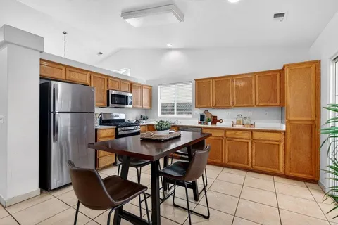 a kitchen with stainless steel appliances granite countertop a refrigerator a sink dishwasher a stove a dining table and chairs with wooden floor