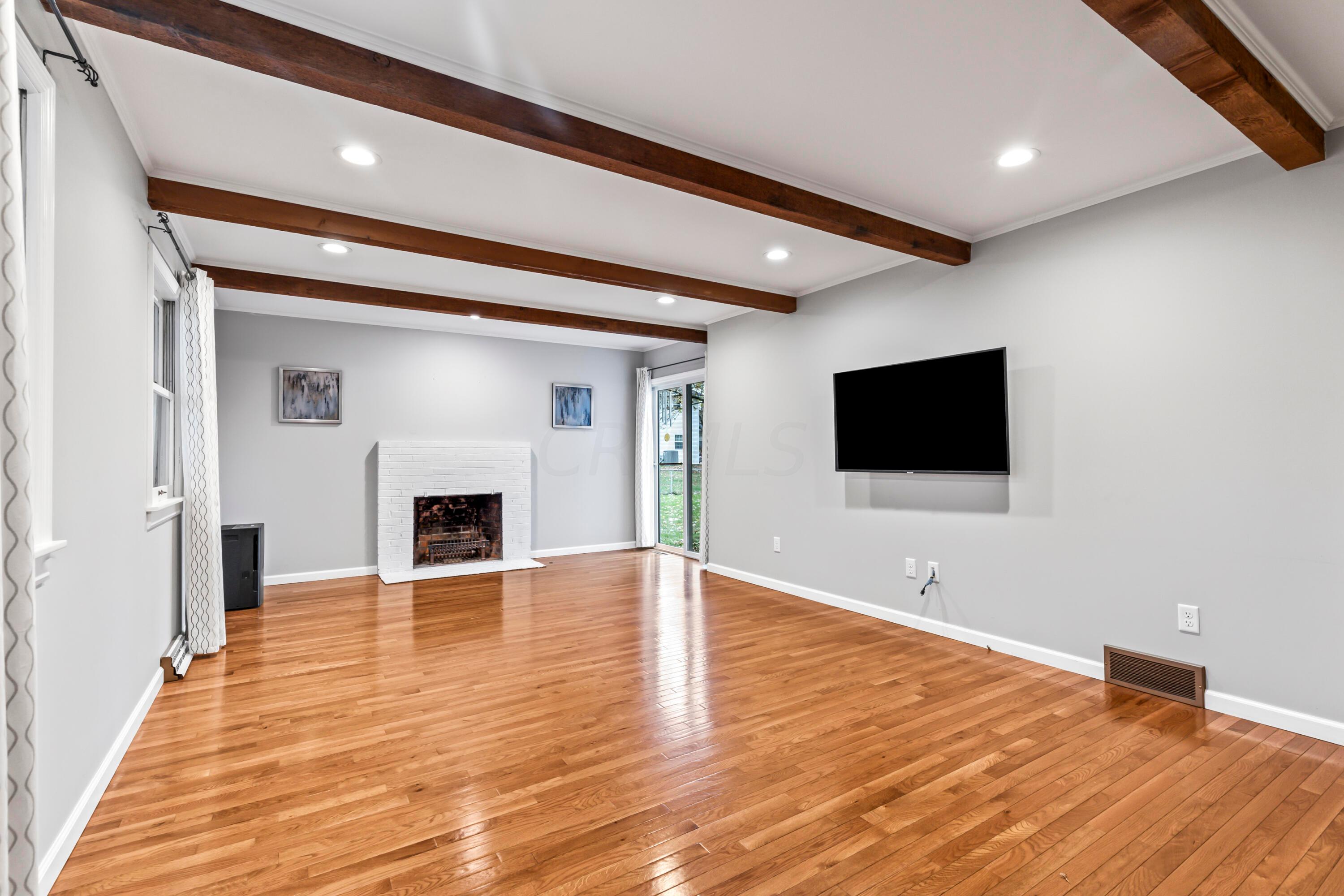 7020 Rieber Street Columbus, OH 43085 - Photo 17 of 40 • New hardwood flooring ~ 2017 • Grey painted walls • Decorative ceiling beams • Can lighting • Wood burning, white painted brick fireplace • Drapes are negotiable • New double sliding doors to patio • TV & mount are negotiable