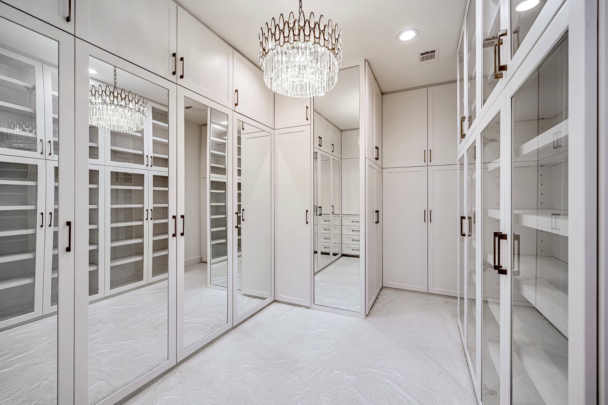 2411 Hazard Street Houston, TX 77019 - Photo 28 of 46 Spacious walk-in closet located in the primary bedroom, featuring custom cabinetry with glass-front doors, a stunning chandelier, and ample drawer storage. The mirror-paneled doors enhance the room's brightness and create a luxurious atmosphere.