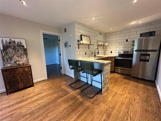 a kitchen with stainless steel appliances kitchen island granite countertop a refrigerator a stove top oven and a dining table with wooden floor
