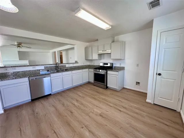 a large kitchen with stainless steel appliances granite countertop a stove top oven a sink dishwasher and white cabinets with wooden floor