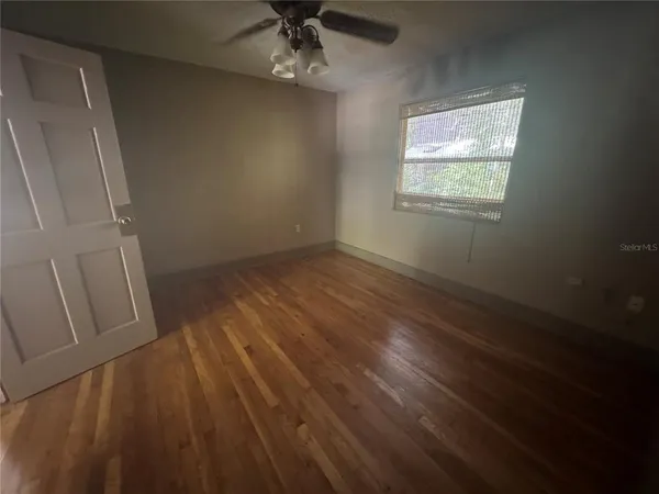 an empty room with wooden floor fan and windows