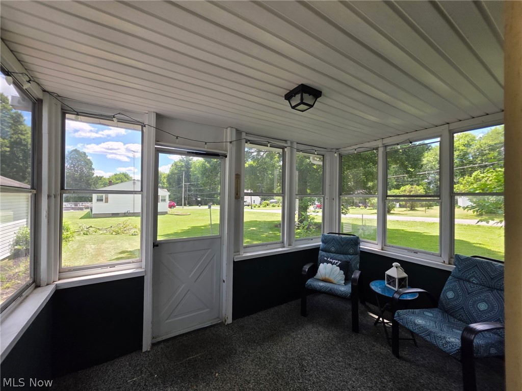 2335 West River Road Newton Falls, OH 44444 - Photo 26 of 36 Enclosed porch featuring multiple windows, a white paneled door, dark lower wall panels, a textured floor, and a flush-mount ceiling light fixture
